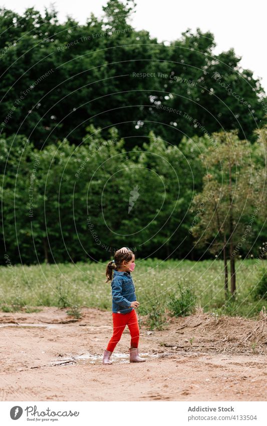 Curious girl surgical mask playing in mud puddle child having fun curious kid rubber boot cute dirty water wet adorable childhood joy activity playful ripple