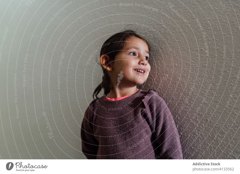 Content ethnic girl near stone wall street adorable child cheerful kid childhood casual smile sweater happy joy charming cute relax urban carefree tranquil