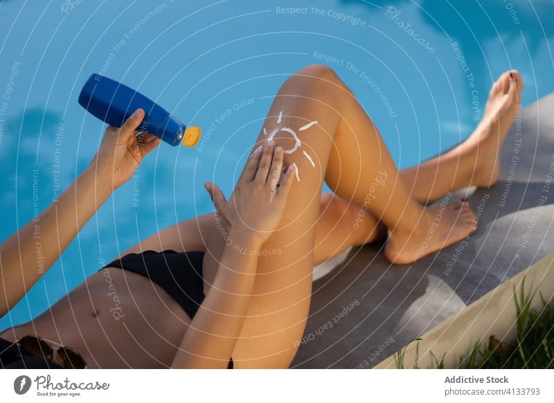 Woman applying sunscreen near pool woman sunbath poolside summer tan cream female leg relax rest holiday suntan recreation summertime protect swimwear swimming