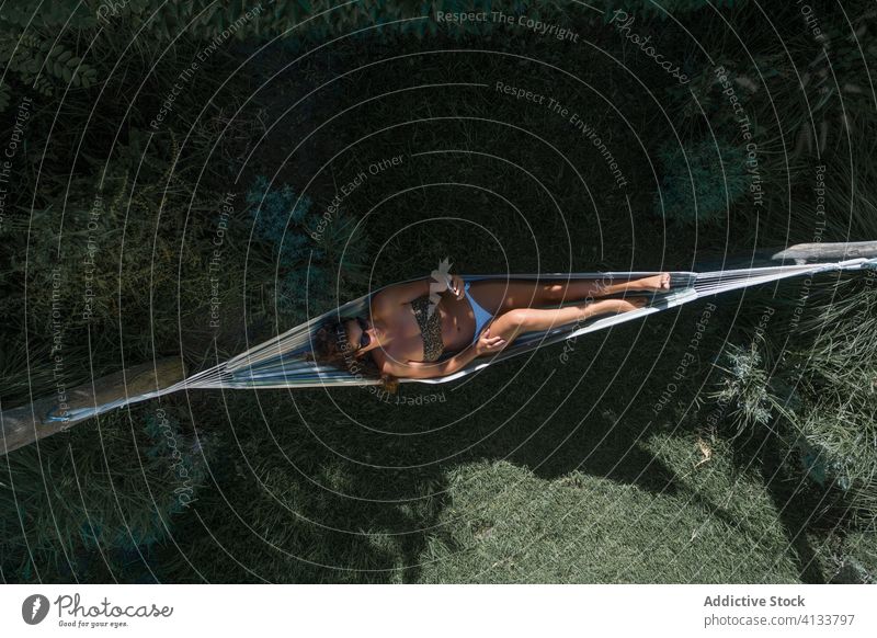 Woman relaxing in hammock in garden with mobile phone woman happy lying summer carefree chill enjoy weekend pleasure glad satisfied wellness bikini female rest