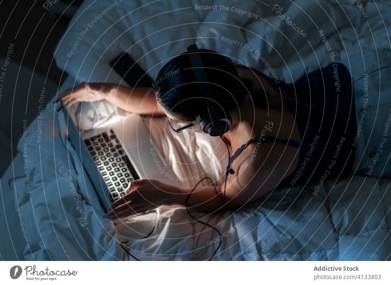 Woman listening to music with headphones in the computer on bed relax woman enjoy using song female browsing blanket lying down tank top device technology