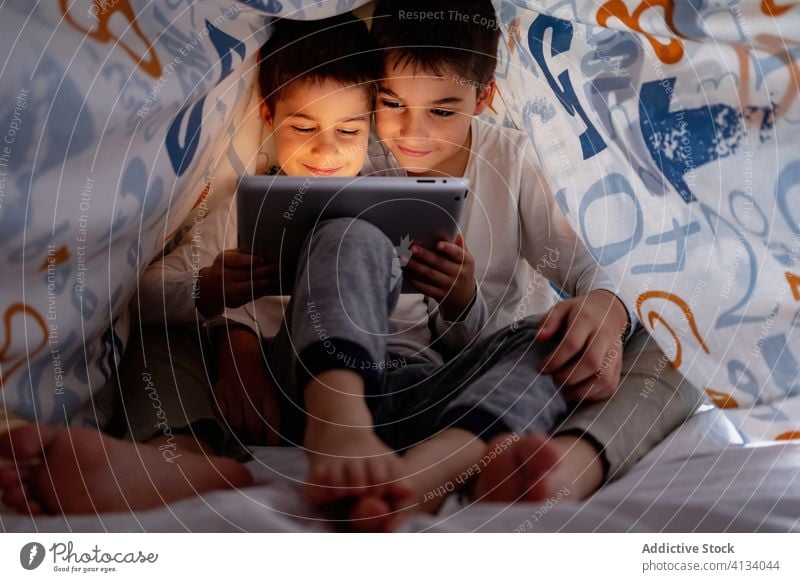 Happy brothers watching video on tablet together cartoon sibling browsing pajama blanket using hide enjoy home daytime interesting positive kid bed boy