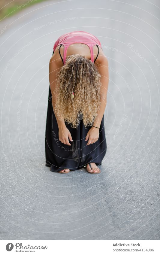 Tired woman performing forward bend on road stretch summer tired nature countryside exhausted female roadway stand relax casual outfit vitality wellness