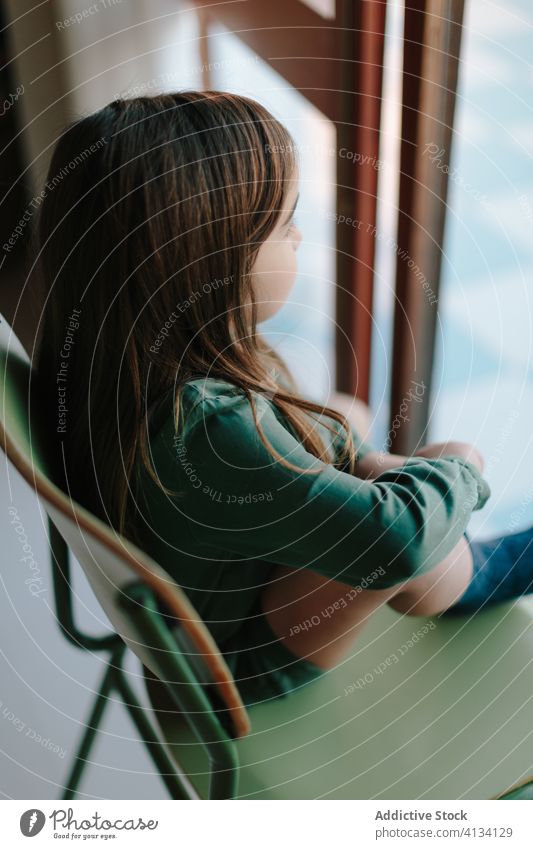 Dreamy girl sitting on chair near window thoughtful child observe relax street kid pensive dreamy calm home contemplate rest adorable cute think childhood