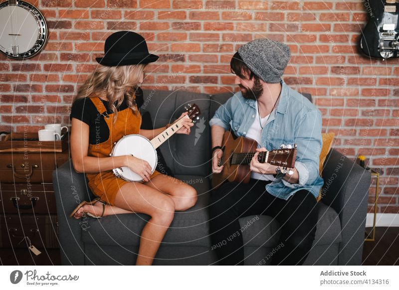 Cheerful couple playing guitar and banjo sitting on sofa music free time duet relationship friendship together legs crossed musical instrument boyfriend slim