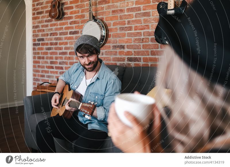 Musician playing guitar sitting with girlfriend on sofa at home couple music free time comfort living room friendship together relationship legs crossed