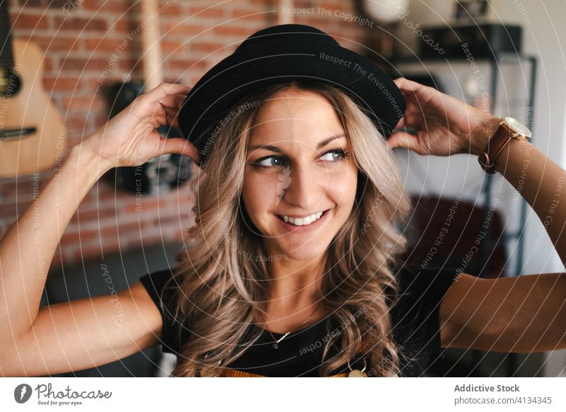 Positive woman in black hat in apartment hipster happy toothy smile free time slim loft design home sofa glad positive charismatic slender casual sundress flat