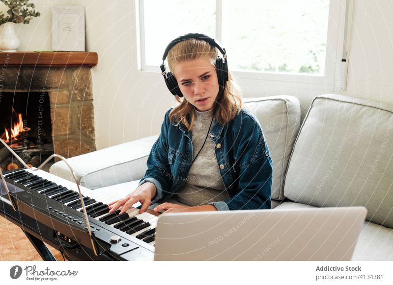 Young woman playing synthesizer at home piano learn online music electronic musician laptop tutorial young composer female modern device gadget hobby lifestyle