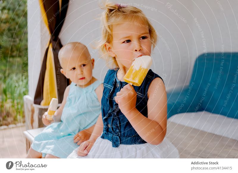 Content sisters eating homemade ice lollies on terrace popsicle lolly girl kid together yummy toddler little delicious sweet cute courtyard tasty dessert