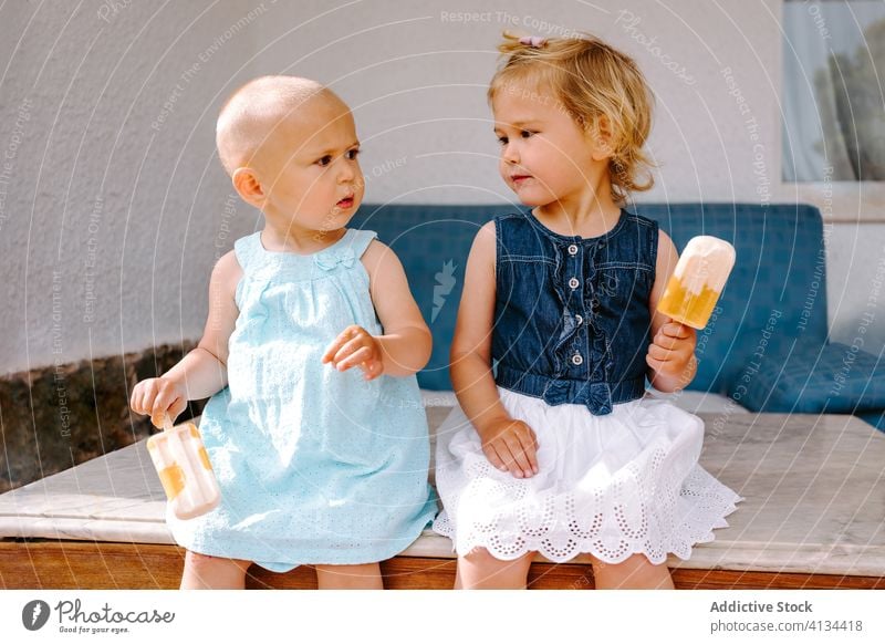 Content sisters eating homemade ice lollies on terrace popsicle lolly girl kid together yummy toddler little delicious sweet cute courtyard tasty dessert