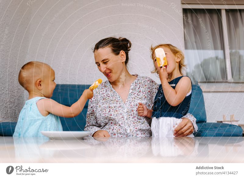 Delighted grandmother and little girls eating ice cream on terrace popsicle enjoy granddaughter together courtyard homemade delight woman cheerful toddler smile