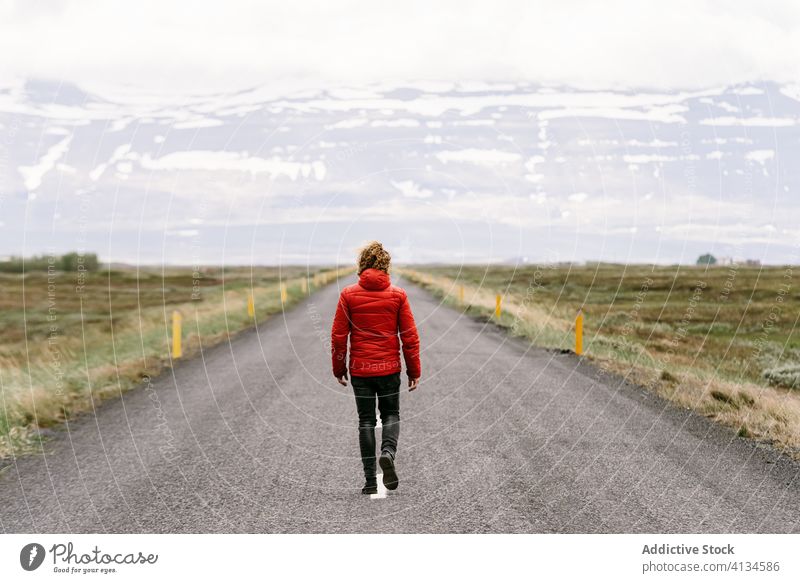 Lonely anonymous male tourist walking along road traveler mountain man roadway scenic asphalt winter iceland empty scenery nature adventure snow cold season