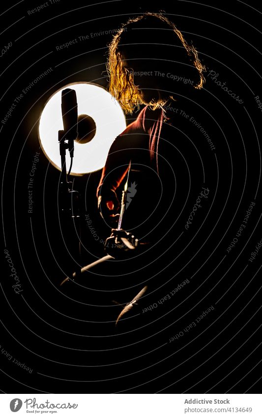 Male musician playing guitar in dark studio guitarist man silhouette microphone glow lamp male skill rock creative talent light luminous illuminate perform