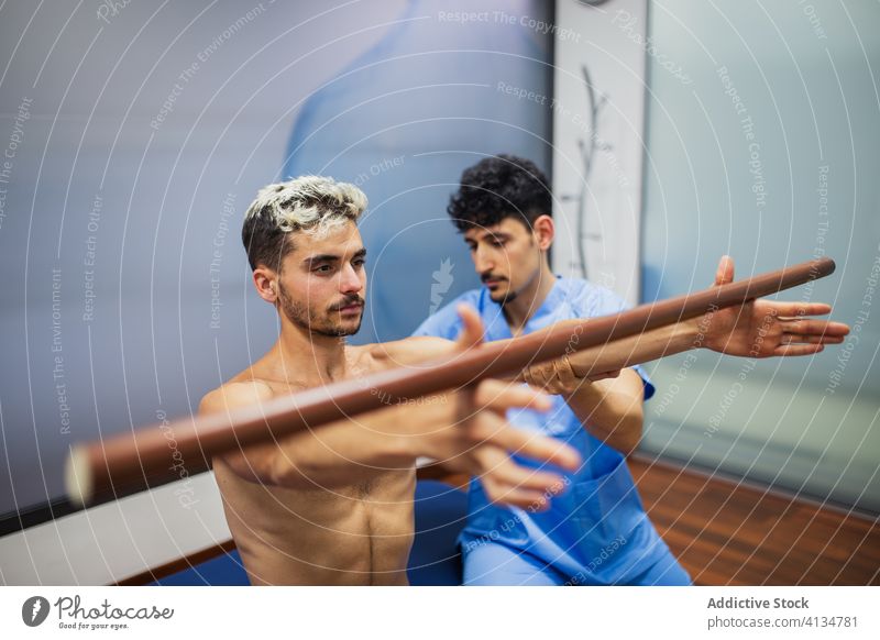 Orthopedist with sportsman holding stick during rehabilitation process in clinic chiropractor patient assistance health care recovery osteopathic check up