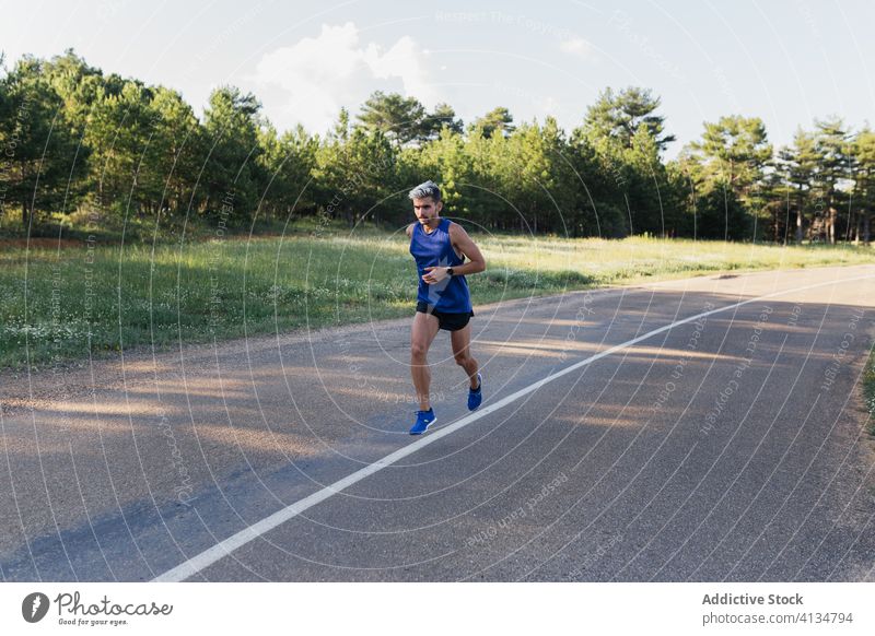 Determined man running on road during workout training fast exercise fitness young sport activity sportswear jog urban healthy body slim strong power