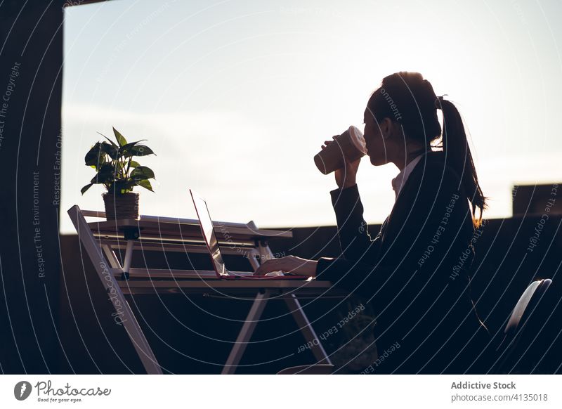 Young woman with laptop drinking coffee on rooftop work break busy pensive entrepreneur remote asian female young formal takeaway cup device gadget beverage