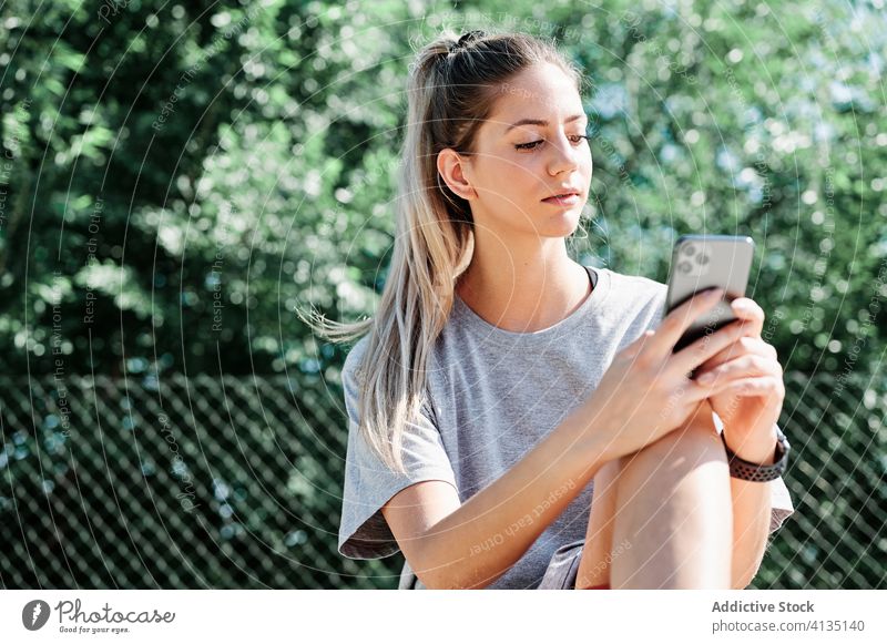 Sportswoman with basketball ball using smartphone on playground court serious young rest browsing mobile sport sportswoman athlete training activity player