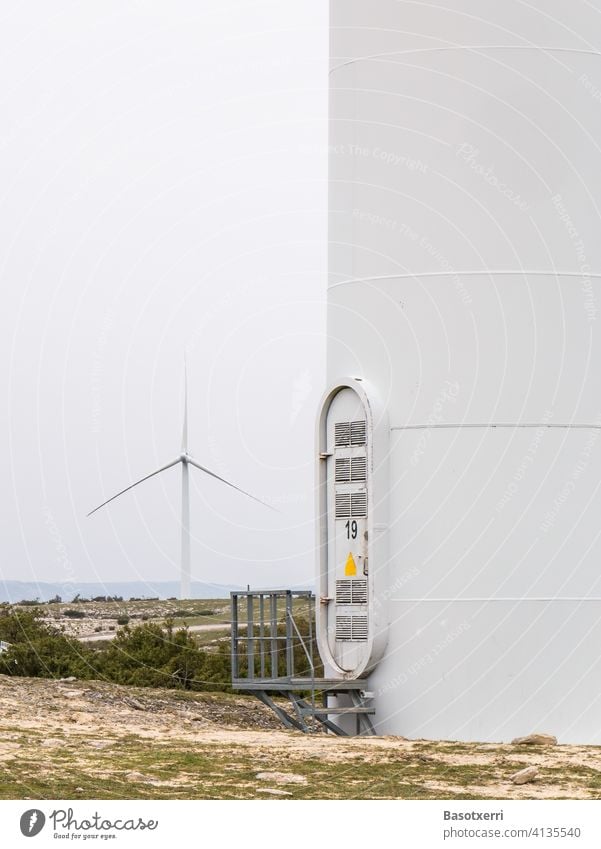 Close-up of a wind farm in the mountains of northern Spain - tower with entrance/ascent, another wind turbine in the background Wind energy plant Tower Entrance