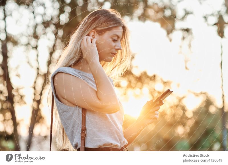 Happy woman with smartphone standing in park cheerful using happy enjoy browsing young female trendy lifestyle gadget device rest chill positive social media