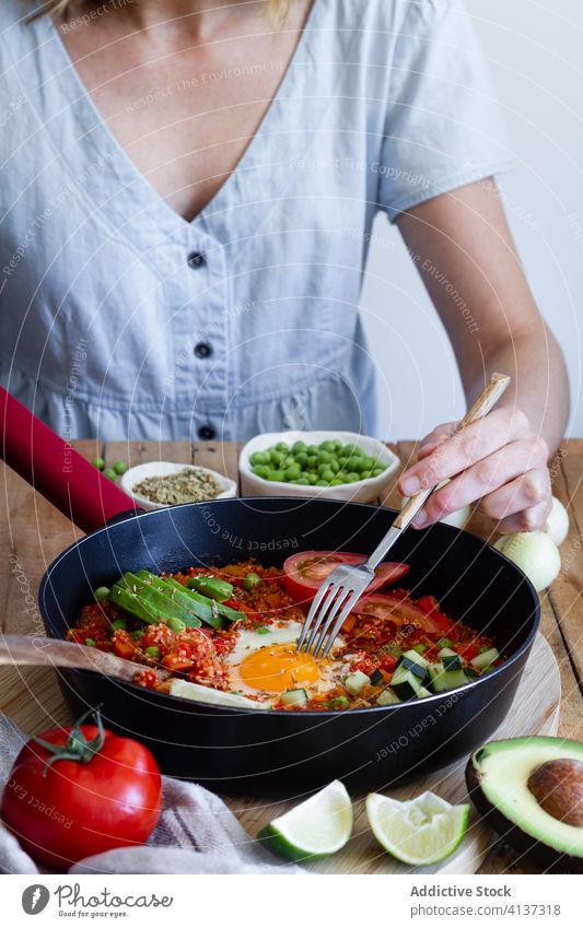 Crop woman eating tasty shakshuka in kitchen egg vegetable enjoy breakfast ingredient dish pan calorie female tradition quinoa tomato sit delicious cuisine