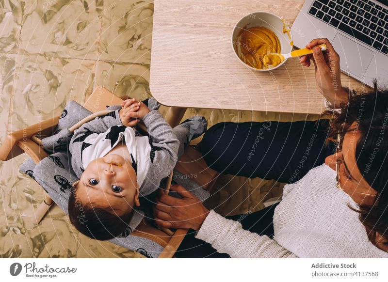 Busy mother feeding kid and working from home woman laptop busy modern connection interact young female baby device gadget child multitask lifestyle freelance