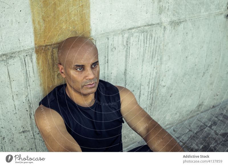 Man resting on stone wall in city relax man sunny shabby exterior male ethnic lean casual daytime staircase guy stairway sunlight shade architecture