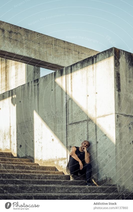 Man resting on stone steps in city relax man stair stroll weathered sunny shabby exterior male ethnic lean wall casual daytime staircase stone wall guy stairway