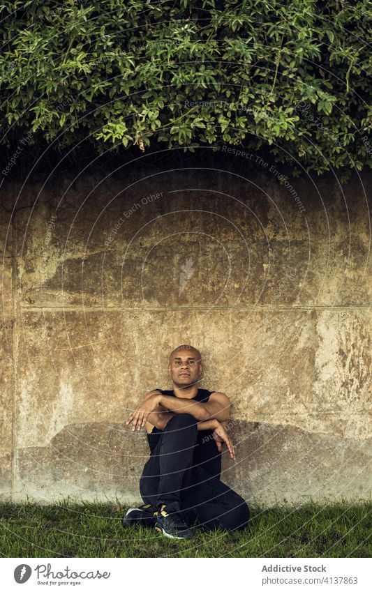 Calm man near wall in park relax weekend garden calm green summer rest male ethnic sit stone grass outfit casual lean nature carefree chill guy enjoy fresh