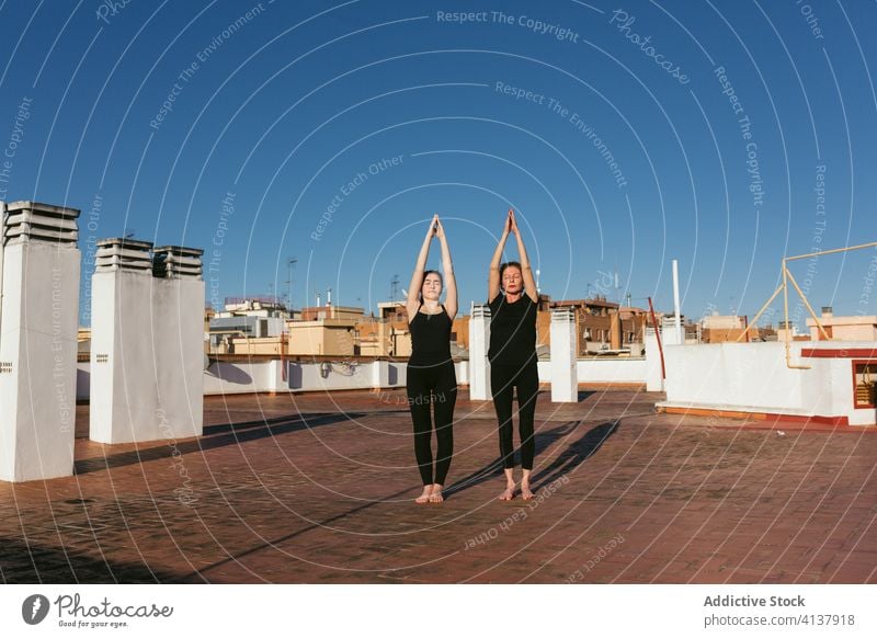 Women performing Sun Salutation during yoga practice women together upward salute sun salutation urdhva hastasana pose stand rooftop position stretch balance