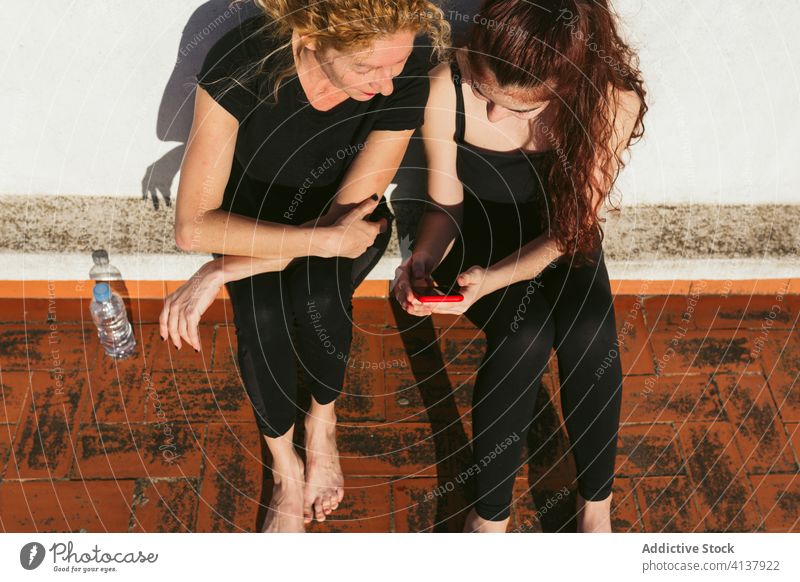 Women with smartphone resting after yoga practice women using cheerful sit mother daughter browsing watch gadget device internet connection online rooftop