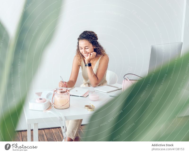 Smiling woman writing in notebook in office notes smiling leaves plant business work table leaning female palma de mallorca spain cheerful happy style elegant