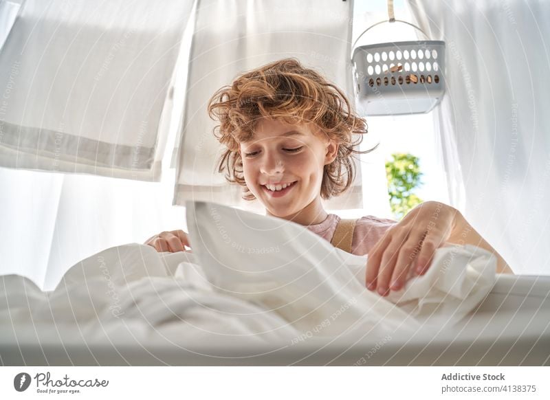 Little boy with basket of linen on balcony at home wash hang laundry domestic chore kid childhood help sit everyday assist clean hygiene care cute happy work