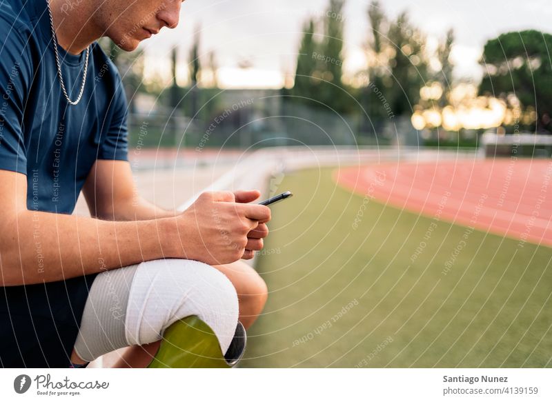 Disabled athlete using phone man runner unrecognized faceless sport prosthesis prosthetic disability disabled amputation amputee anonymous type typing