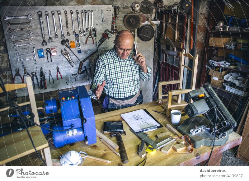 Carpenter in his workshop top view carpenter man mobile senior talking business custom made work bench mature tablet male carpentry writing wood worker plans