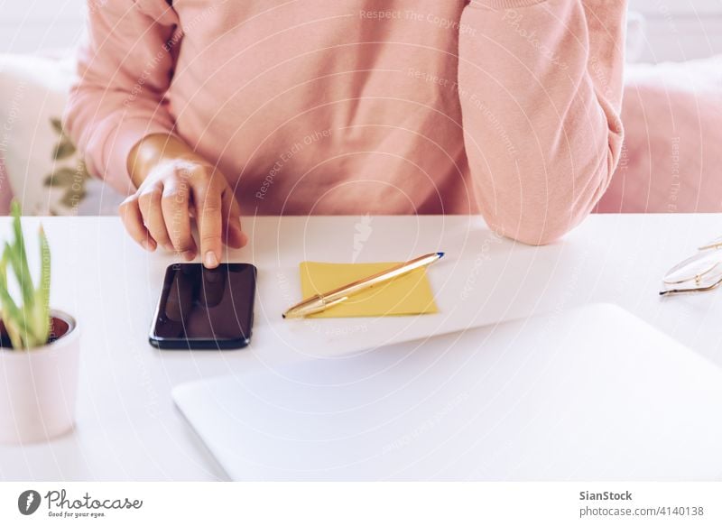 Young woman using mobile phone while working at home with laptop. business technology smart computer desk connection smartphone workplace freelancer message