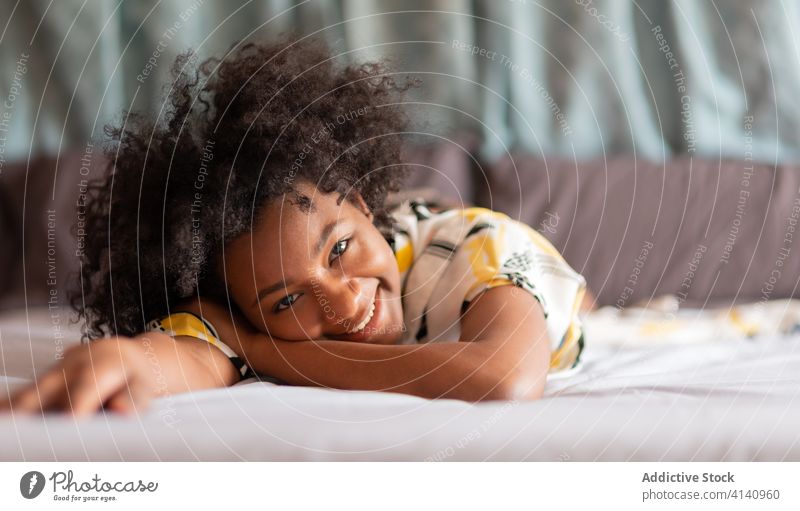 Cheerful African American woman resting on bed in modern apartment chill home lying smile cheerful cozy female ethnic black african american domestic outfit