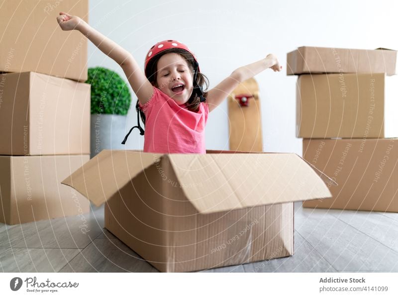 Cheerful girl playing in carton box smile helmet fasten sit moving relocate fun imagination kid child fantasy happy little cute home adorable excited glad