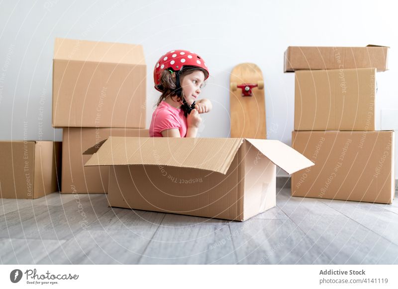 Cheerful girl playing in carton box smile helmet fasten sit moving relocate fun imagination kid child fantasy happy little cute home adorable excited glad