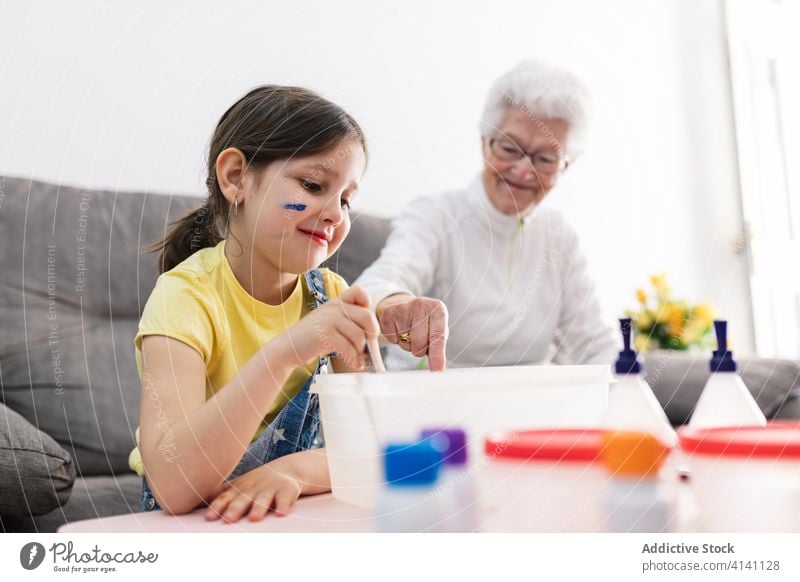 Cheerful grandmother and girl creating slime in container at home granddaughter handcraft fun diy art childcare upbringing preschool domestic together process