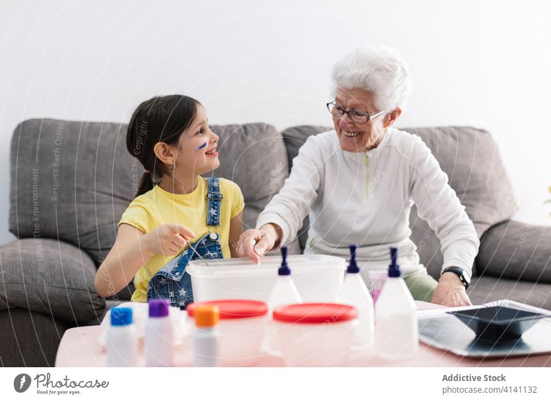 Cheerful grandmother and girl creating slime in container at home granddaughter handcraft fun diy art childcare upbringing preschool domestic together process