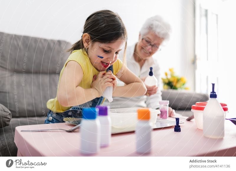 Cheerful grandmother and girl creating slime in container at home granddaughter handcraft fun diy art childcare upbringing preschool domestic together process