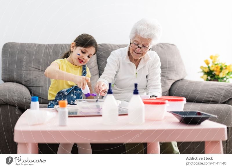 Cheerful grandmother and girl creating slime in container at home granddaughter handcraft fun diy art childcare upbringing preschool domestic together process