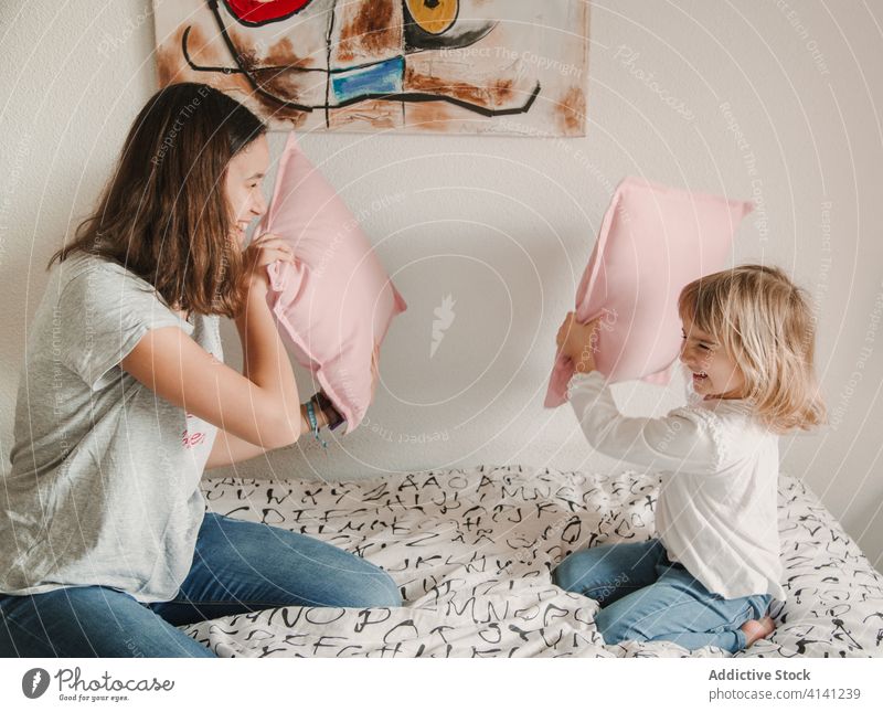 Delighted sisters fighting with pillows on bed playful having fun game girl sibling little teenage cozy together happy childhood home bedroom joy laugh kid