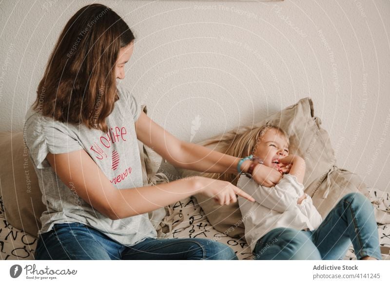 Teenage girl tickling little sister on bed tickle laugh play playful having fun game weekend together cheerful home teen happy cozy joy sibling relative