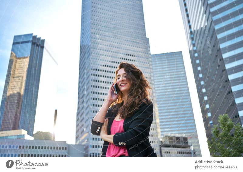 Adult woman talking on smartphone in city businesswoman content elegant speak skyscraper using female center jacket work cellphone conversation call device