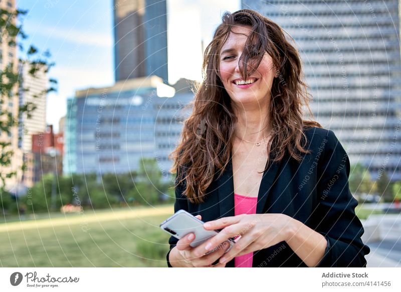 Cheerful businesswoman in jacket browsing smartphone on street entrepreneur using city classy smile urban female mobile device gadget communicate internet