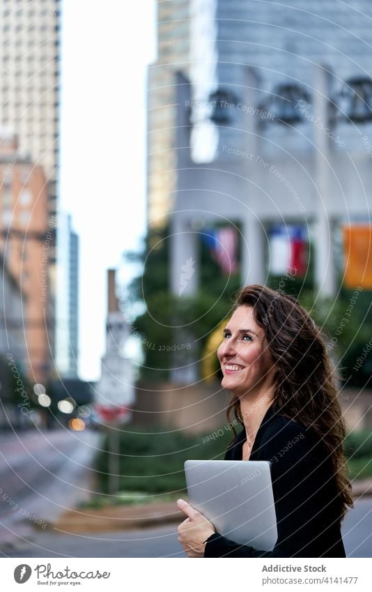 Businesswoman with laptop on city street entrepreneur businesswoman confident cityscape formal well dressed professional female cheerful content smile determine