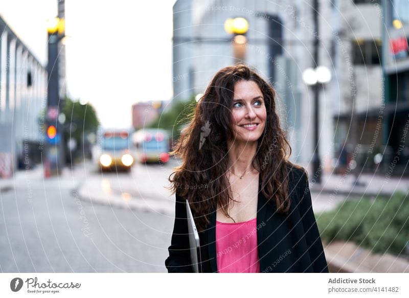 Businesswoman with laptop on city street entrepreneur businesswoman confident cityscape formal well dressed professional female cheerful content smile determine