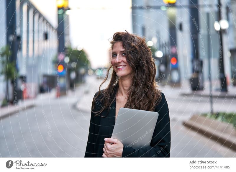 Businesswoman with laptop on city street entrepreneur businesswoman confident cityscape formal well dressed professional female cheerful content smile determine