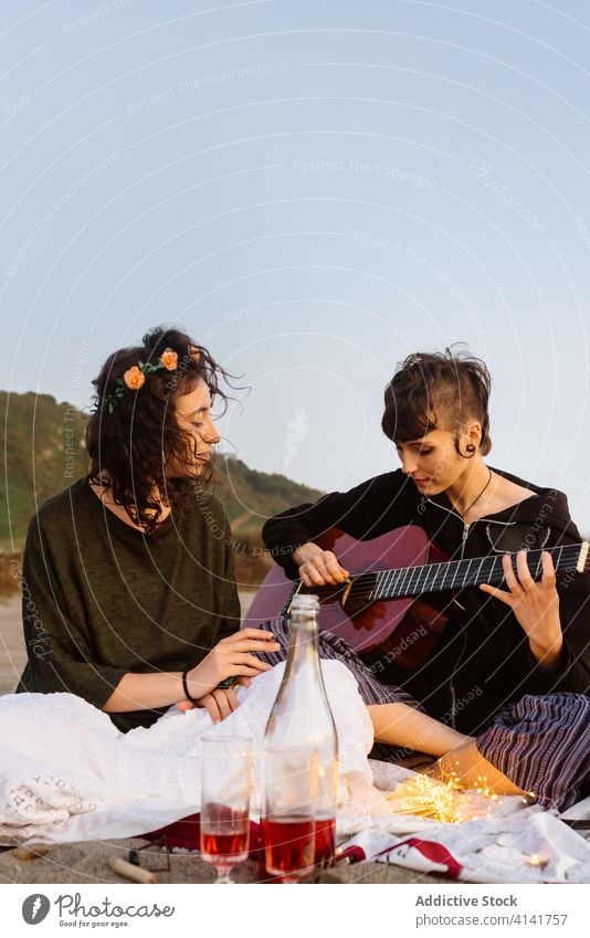 Woman playing guitar for girlfriend on beach lesbian couple picnic music acoustic sunset lgbt seaside instrument together musician romantic relax summer